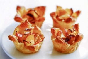Four mini apple tarts made from apple slices in puff pastry shells on a plate