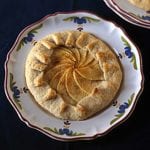 Individual rustic apple tart with the crust folded over a filling of sliced apples on a flowered plate