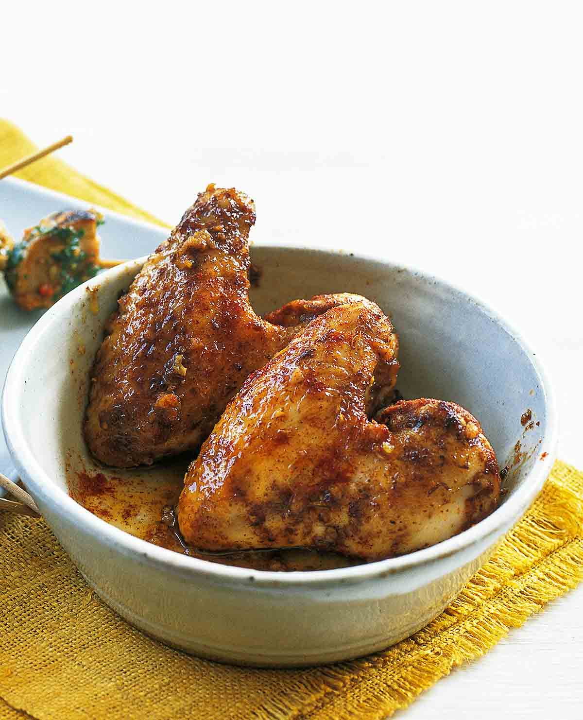 A white bowl with two chicken wings with garlic and paprika on a yellow placemat.