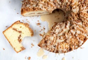 A whole sour cream coffee cake with a wedge cut from it.