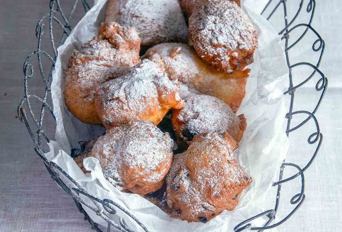 Oliebollen, or Dutch doughnuts, in a wire basket, covered with powdered sugar on a white tablecloth.