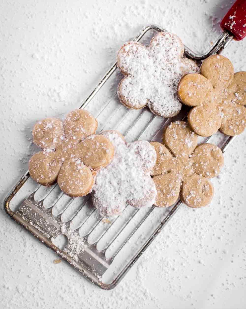 A kitchen tool with five flower-shaped Chinese five-spice cookies topped with powdered sugar