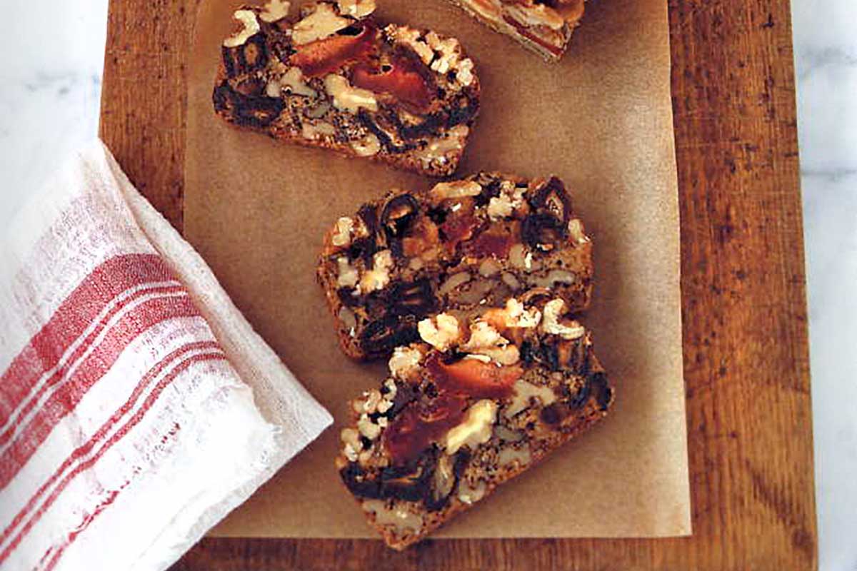 Dried fruit and nut cake cut into three slices on a cutting board on marble