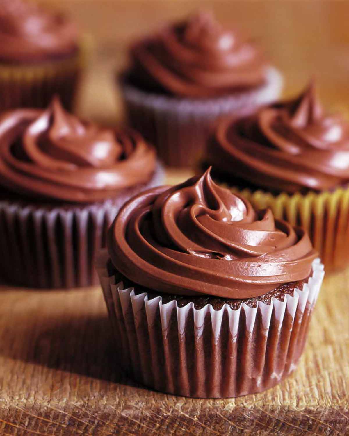 Five chocolate orange cupcakes with swirls of chocolate frosting on top.