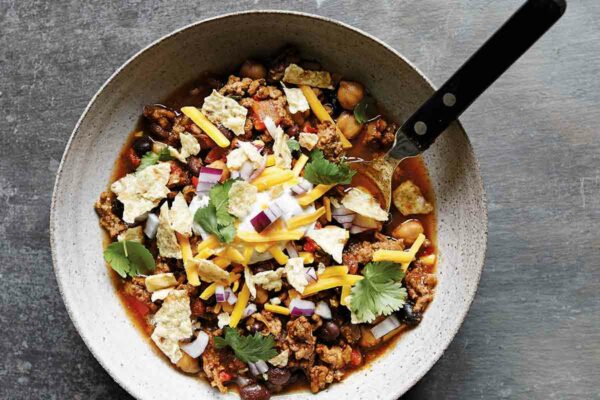A pottery bowl of slow-cooker beef chili from Skinnytaste, topped with tortilla chips, cilantro, red onions, and cheese.