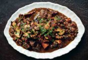 A white platter with beef Bourguignon, filled with beef, carrots, and mushrooms
