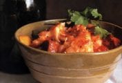 A brown ceramic bowl filled with Portuguese fish chowder, made with fish, potatoes, chouriço, tomatoes, and cilantro.