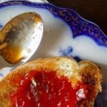 A slice of toast schmeared with Portuguese tomato jam on a decorative plate with a spoon resting beside it.