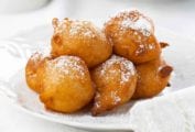 A pile of ricotta-sweet potato beignets dusted with confectioners' sugar on a white plate.