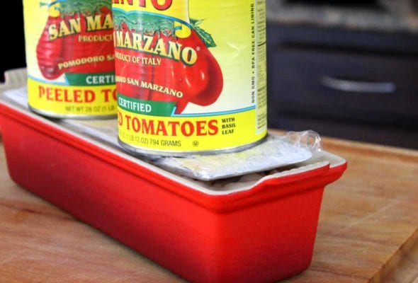 A red terrine mould filled with country pate, being weighed with two cans of tomatoes