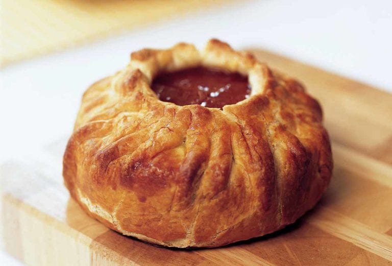 A wheel of brie cheese baked pastry, on top is a dollop of apricot preserves
