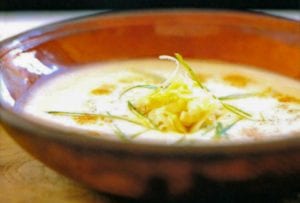 Brown bowl of spicy Swiss potato soup with scallion, Gruyere cheese, and potatoes on top