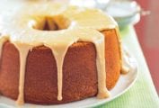 A frosted brown sugar pound cake on a white plate on a cloth-covered picnic table.