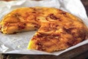 A potato pancake, with cheese and bacon, with a slice missing, on crumpled parchment