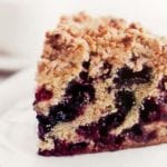 A slice of blueberry buckle with layers of blueberries and a crumb topping of butter, flour, sugar, cinnamon, and ginger