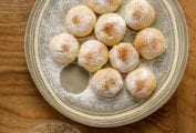 A plate of round Greek biscuit cookies with an apple filling, all dusted with powdered sugar