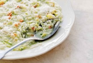 A bowl filled with zucchini risotto and a spoon resting inside.