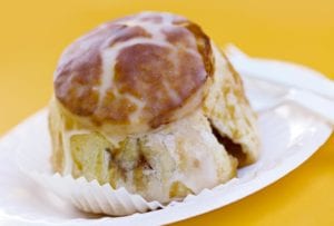 A large glazed apple dumpling on a white plate against a yellow background