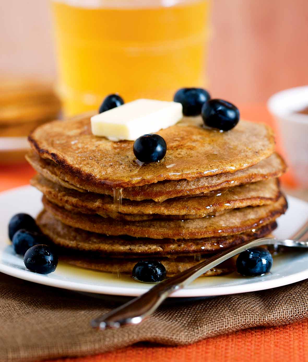 Gingerbread pancakes stacked on a plate, covered with syrup, blueberries, and a pat of butter.