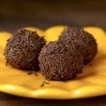 Three golf-ball size chocolate Brazilian candies covered with chocolate sprinkles on a yellow plate