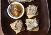 Wedges of Arlington chicken liver pate on top of crisp crackers on a brown serving platter along with a small bowl of chutney.