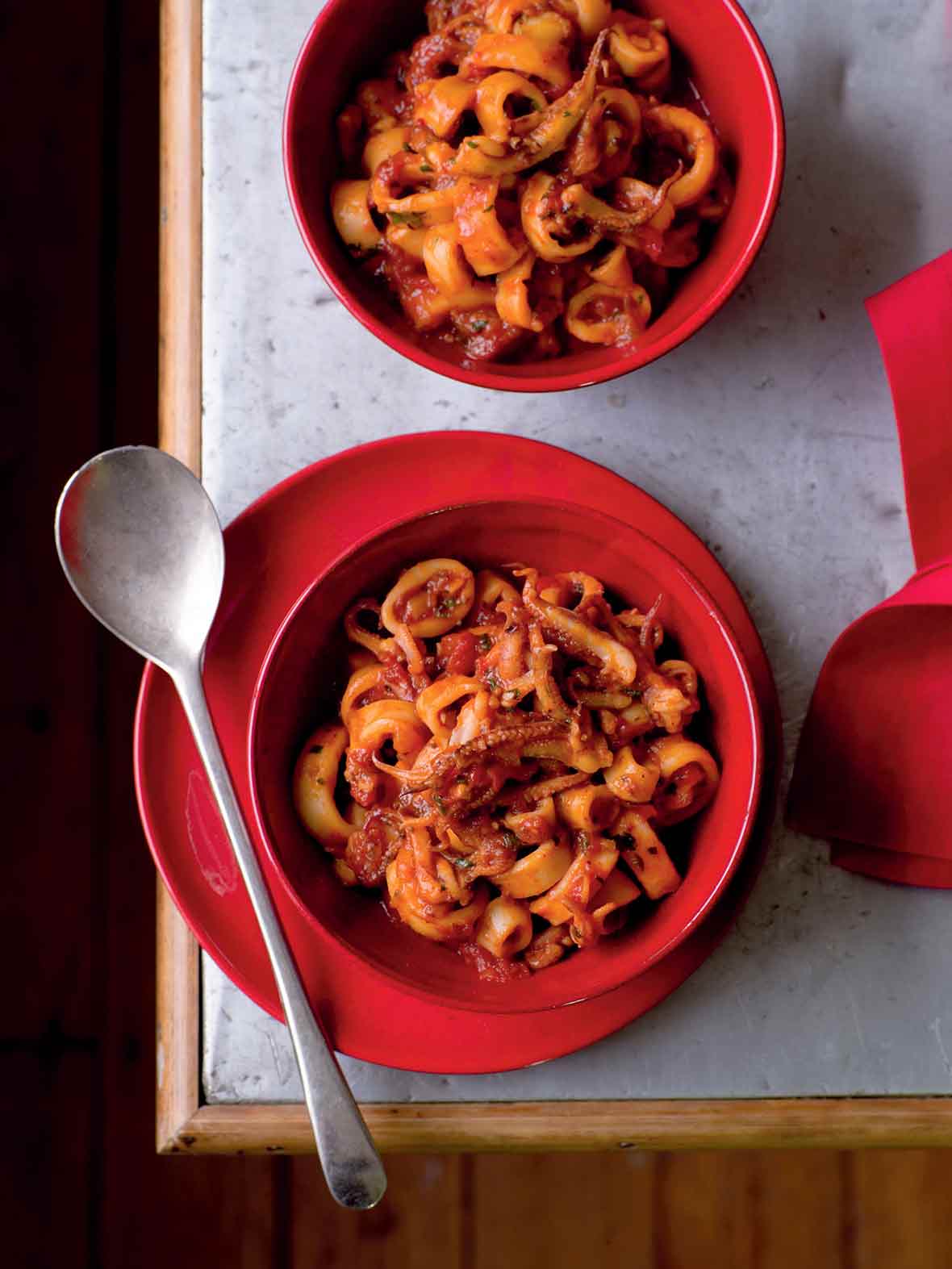 A red bowl with Christmas Eve calamari--calamari, onion, garlic, red pepper flakes in a tomato sauce