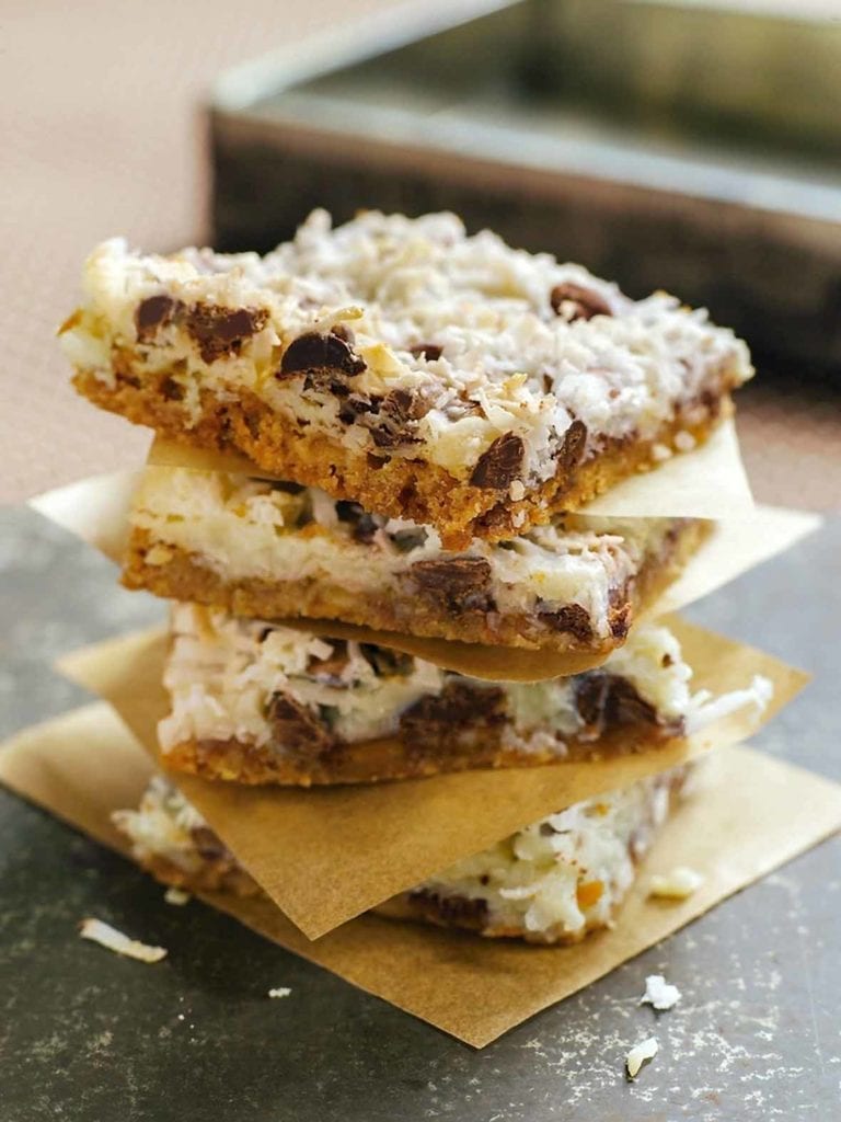 Stack of four Congo bars made of coconut, chocolate, graham crackers, each on a square of paper