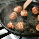 A cast-iron skillet with eight cheater's chorizo meatballs being cooked in it.