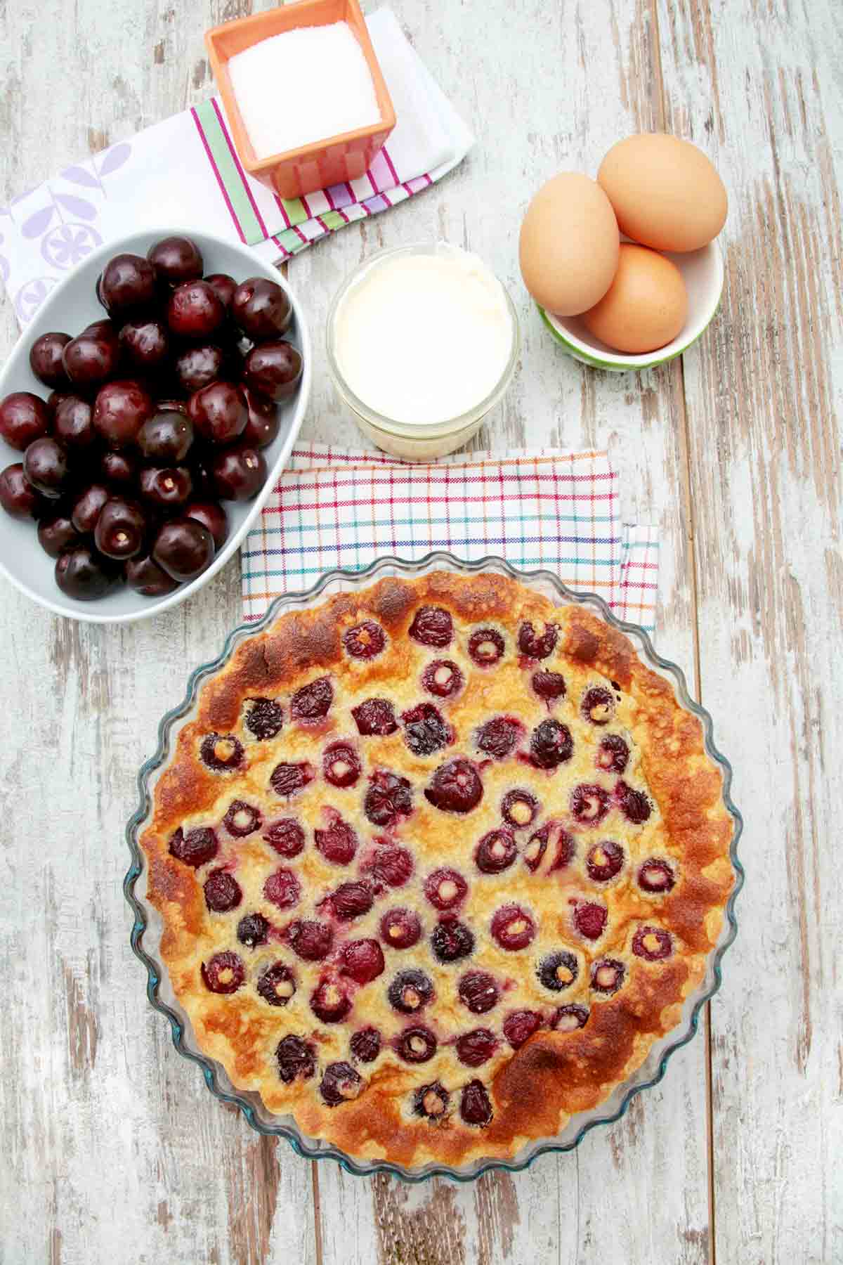 A cherry clafouti and dishes of cherries, eggs, milk, and sugar.