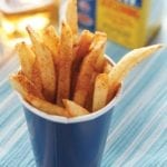 A blue paper cup filled with beach fries that are sprinkled with Old Bay seasoning.