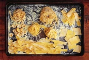 Several shapes of fresh homemade egg pasta dough on a rimmed baking sheet.