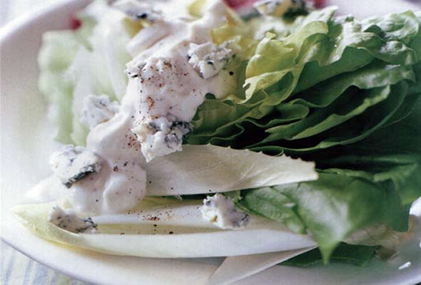 A white plate with a wedge of lettuce, covered with creamy blue cheese dressing.