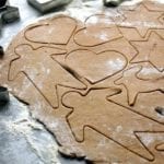 a sheet of raw black pepper cookie dough with shapes--men, stars reindeer, hearts--cut into it