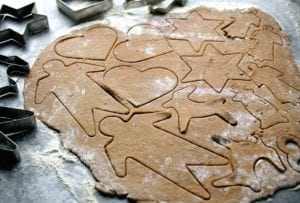 a sheet of raw black pepper cookie dough with shapes--men, stars reindeer, hearts--cut into it