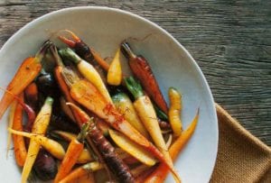 A white bowl of braised saffron carrots on a piece of burlap on a wooden table.