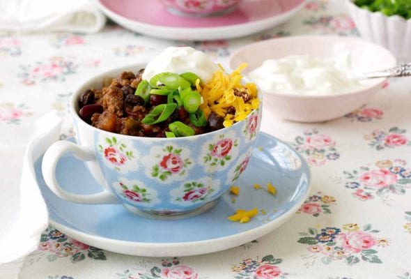 A pretty saucer and teacup filled with game day chili, and topped with scallions, Cheddar, and sour cream.