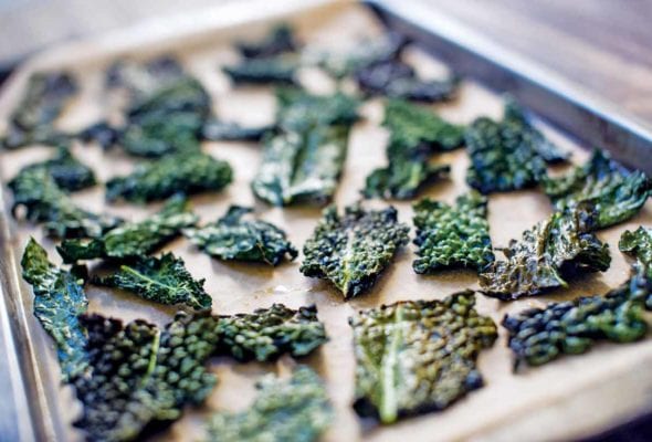 A rimmed baking sheet filled with crispy baked kale chips.