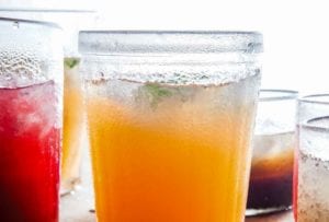 A glass filled with cantaloupe agua fresca, and glasses of other liquid around it.