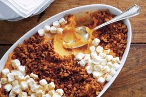 A white casserole dish filled with gingersnap and sweet potato casserole, topped with mini marshmallows and a spoon resting inside.