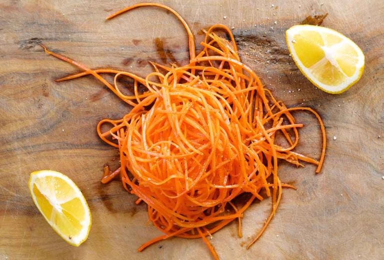 A grated carrot salad piled on a wooden cutting board with two lemon wedges.