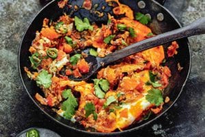 A skillet filled with spicy scrambled eggs with a wooden spoon inside.