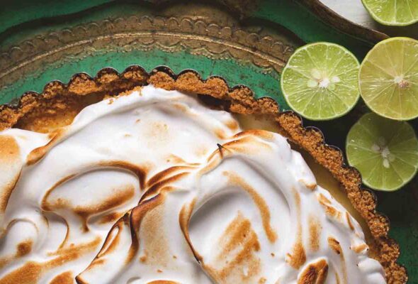 A classic key lime pie with a meringue top and several sliced limes nearby