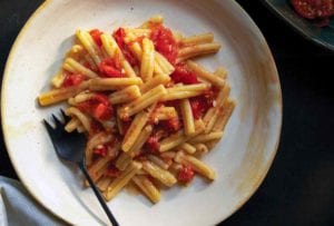 A white plate with cavatelli past topped with a roasted tomato sauce, fork on the side