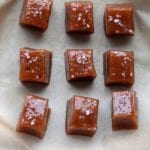 Six square caramels topped with sea salt sitting on a sheet of parchment.