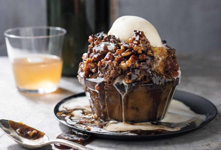 Glass bowl filled with pecan pie bread pudding, caramel sauce, bourbon-vanilla ice cream on a marble table