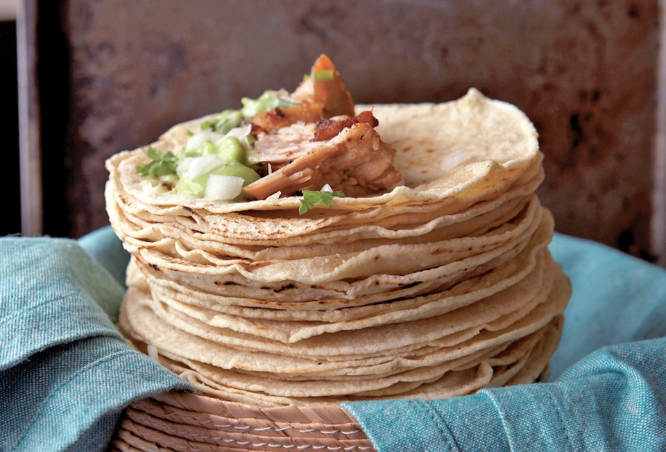 A stack of flour tortillas topped with pork for carnitas tacos.