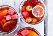 Three glasses filled with rose sangria, lime wheels, nectarine wedges, watermelon cubes, and raspberries.