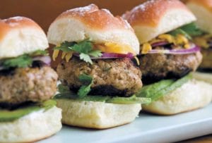 Three small turkey burgers with onions, parsley, avocado on a white plate