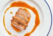 A sliced duck breast with maple bourbon sauce drizzled around it on a blue-rimmed white plate.