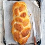A loaf of braided challah bread on a baking sheet with a serrated knife